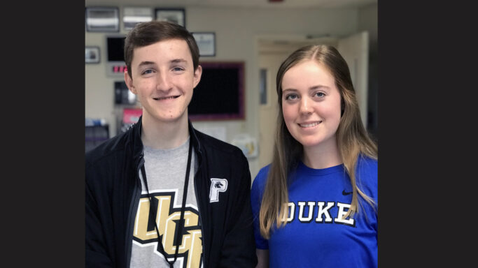 Two seniors standing next to each other in a classroom, recognized for their National Merit Scholarship achievements.