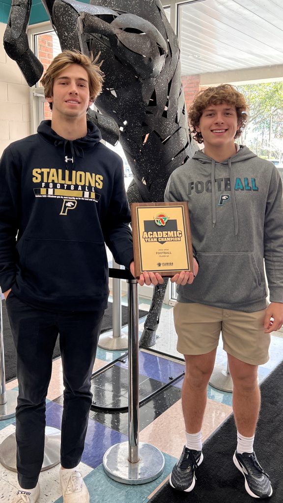 Two young men, one holding a 3A Academic Champion plaque, standing in front of a statue.