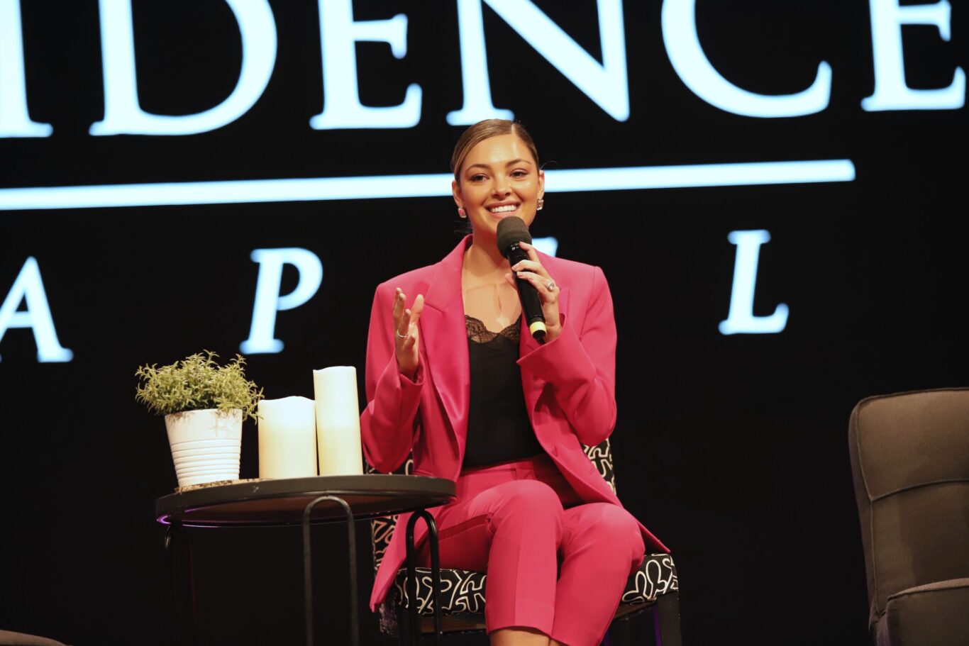 Demi Tebow, a woman in a pink suit, is sitting in a chair at a Special Chapel event.