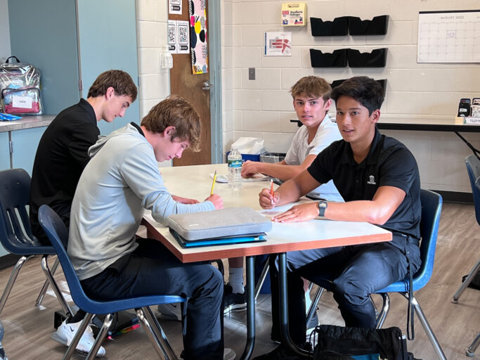 A group of young men sitting at a table in a classroom.