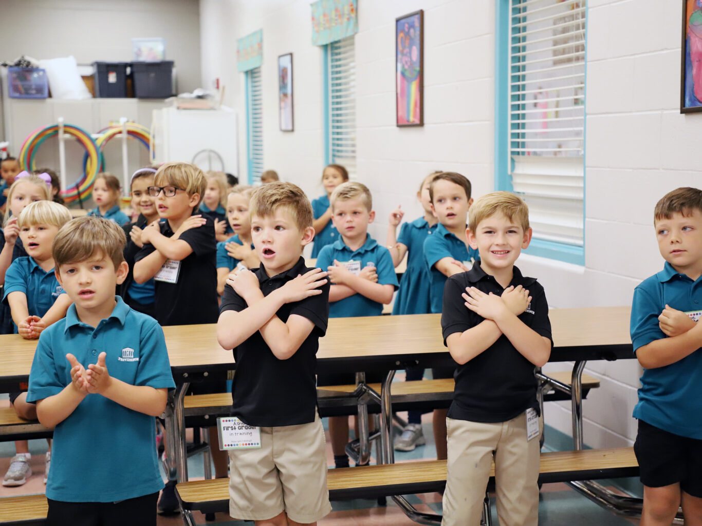 A group of lower school children standing in a classroom and clapping.