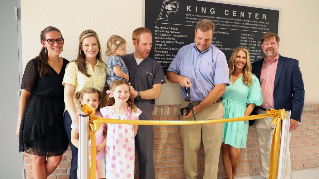 A group of people officially opening the King Center by cutting a ribbon in front of a sign.