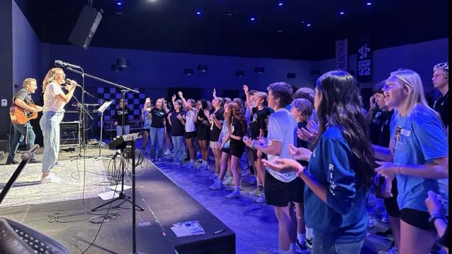 A group of freshman singing in front of a stage at a retreat.