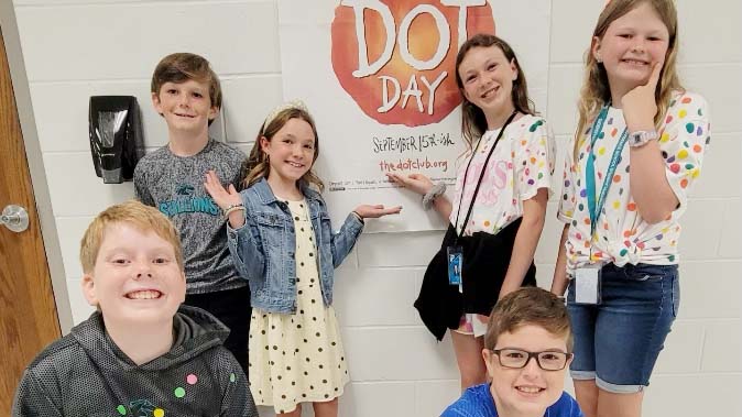A group of international students posing in front of a dot day sign to celebrate.