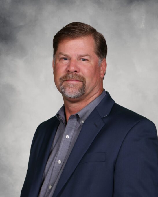 A leadership man in a blue suit standing in front of a gray background.