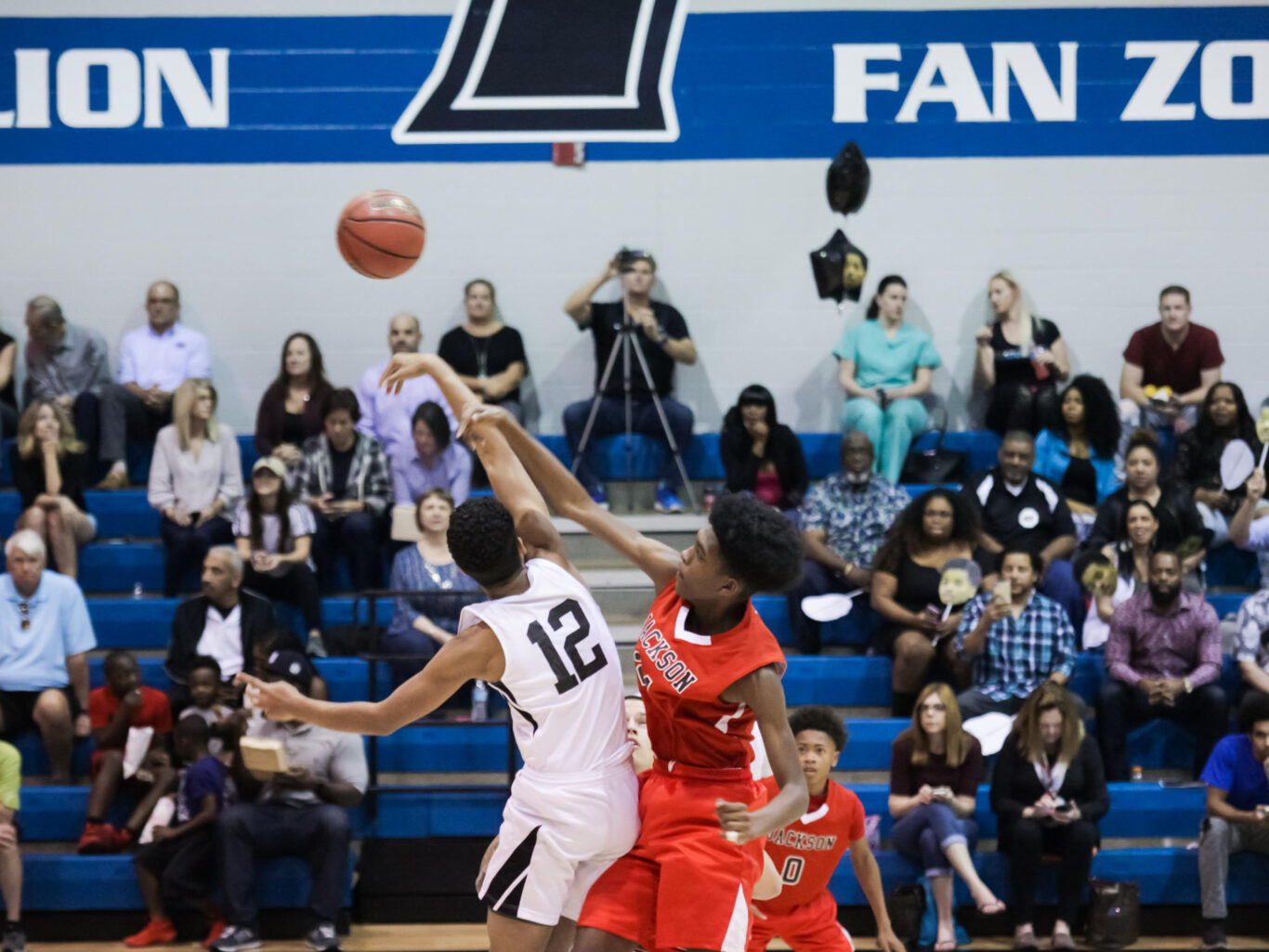 A basketball player is trying to block a shot in front of a crowd at the facilities.