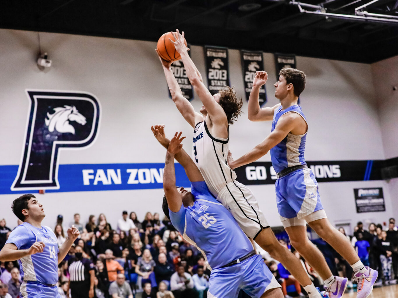 A group of boys playing basketball and trying to block the ball.