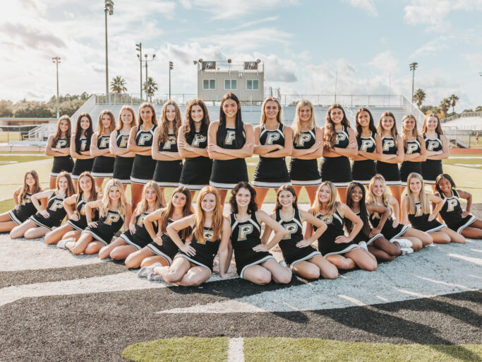 The cheerleaders are striking poses for a photo on a football field, showcasing their athleticism.