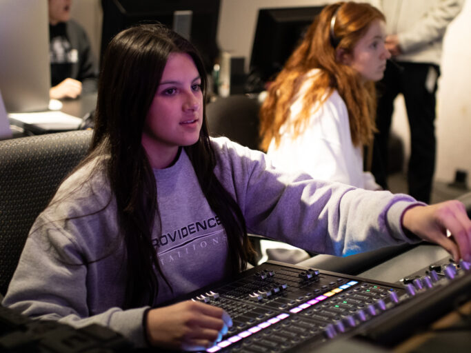 A woman is working on a mixing board in a recording studio.