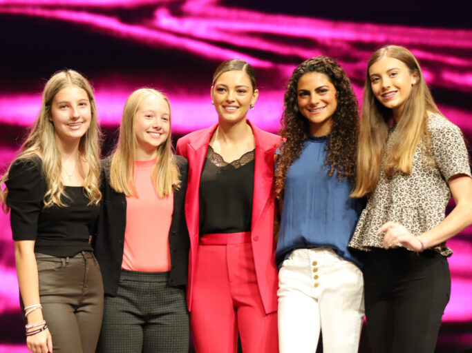 A group of young women, including students, posing for a photo on stage.