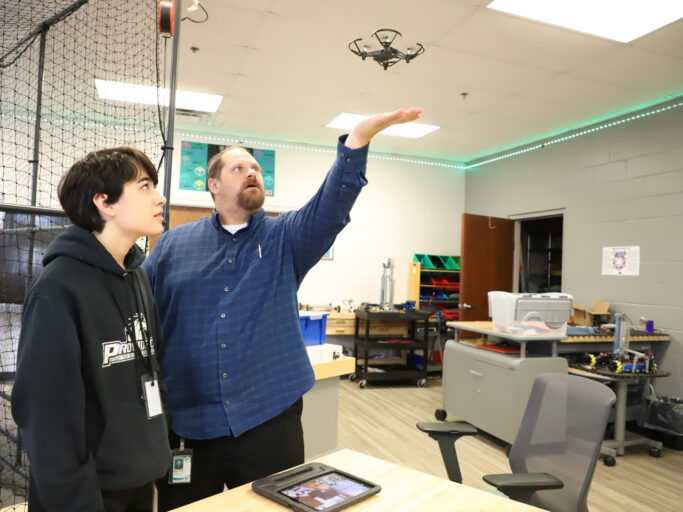 Two men about a drone standing in front of a room.