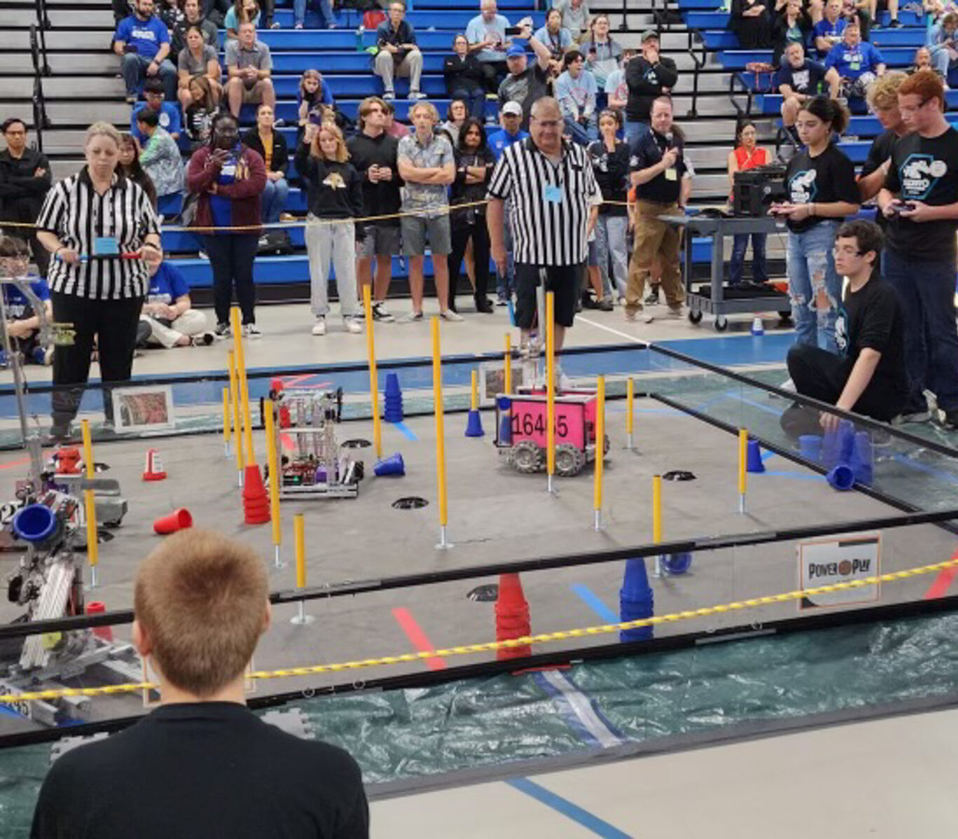 A group of people watching a robotics competition at a Robotics Club.