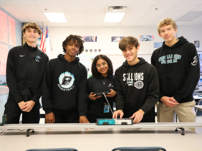 A group of students wearing uniforms standing in front of a table with a robot.