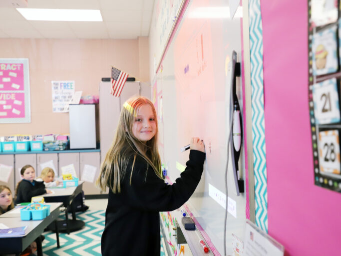 A girl demonstrating her employment skills by writing on a whiteboard in a classroom.