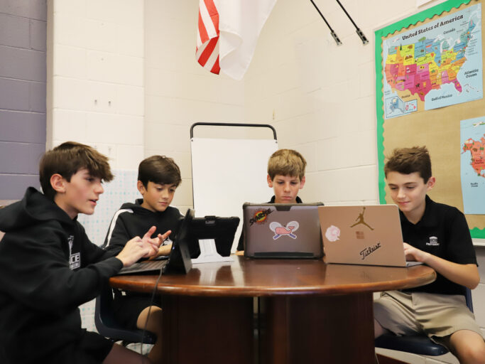 A group of boys utilizing technology with laptops in a classroom.