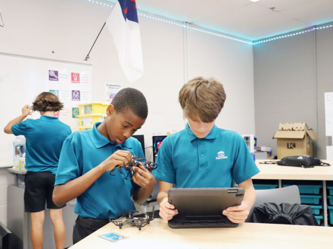 Two student boys working on a tablet in a classroom, showcasing a glimpse of student life.