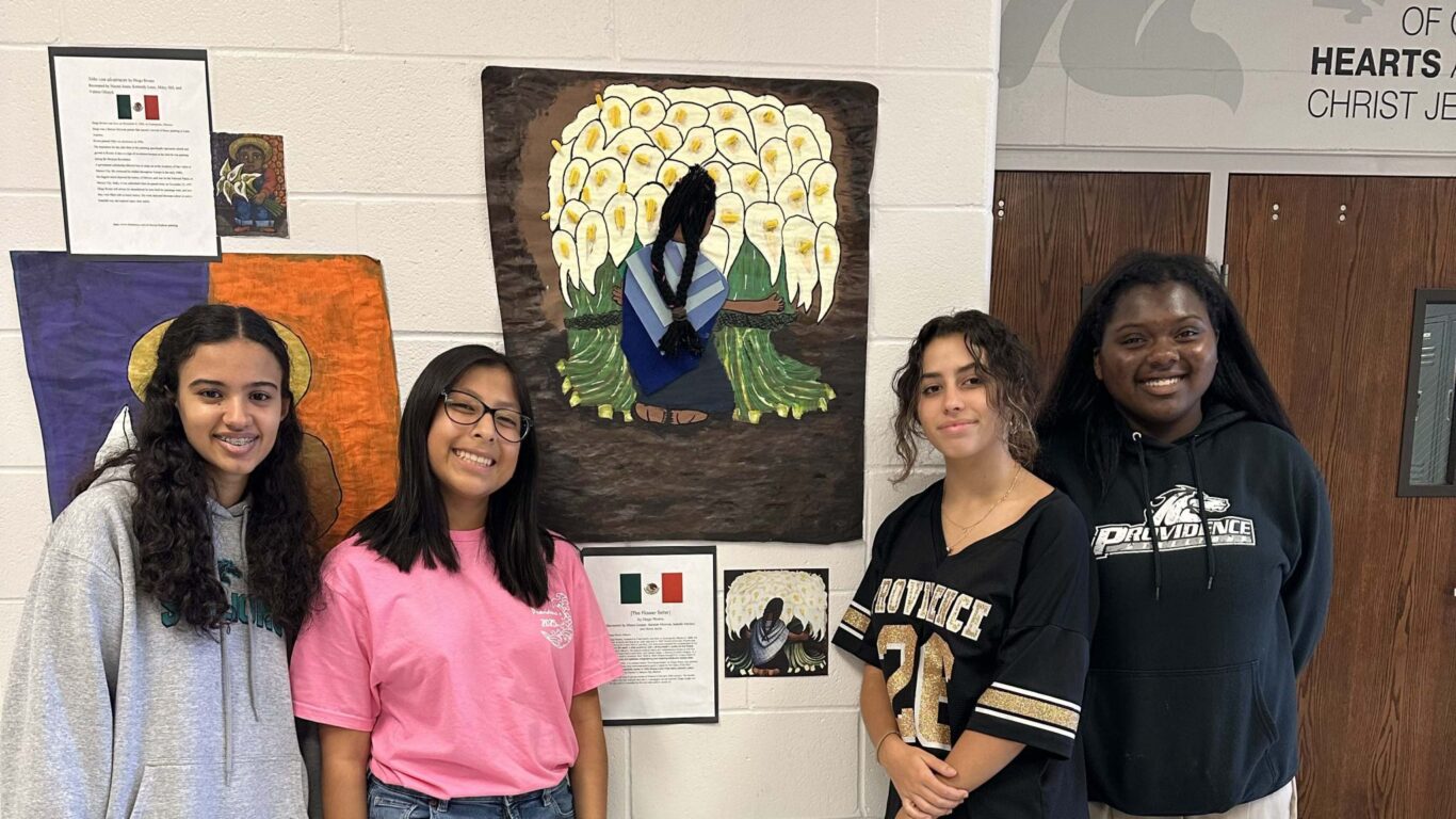 Four Spanish students celebrate in front of a wall with art on it.