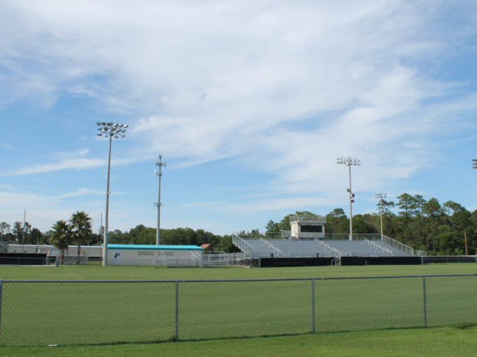 A grassy field with facilities and a fence.