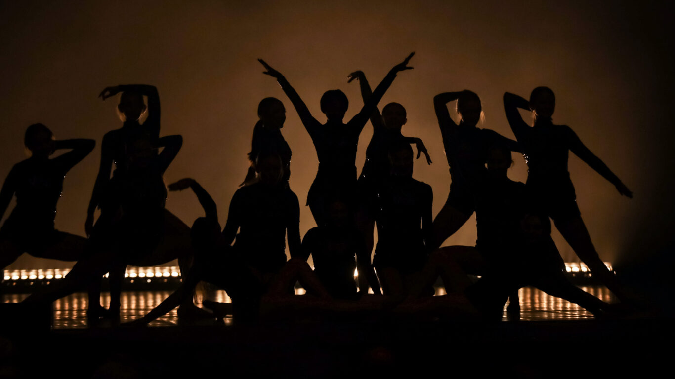 A group of Fine Arts dancers are silhouetted in the dark.