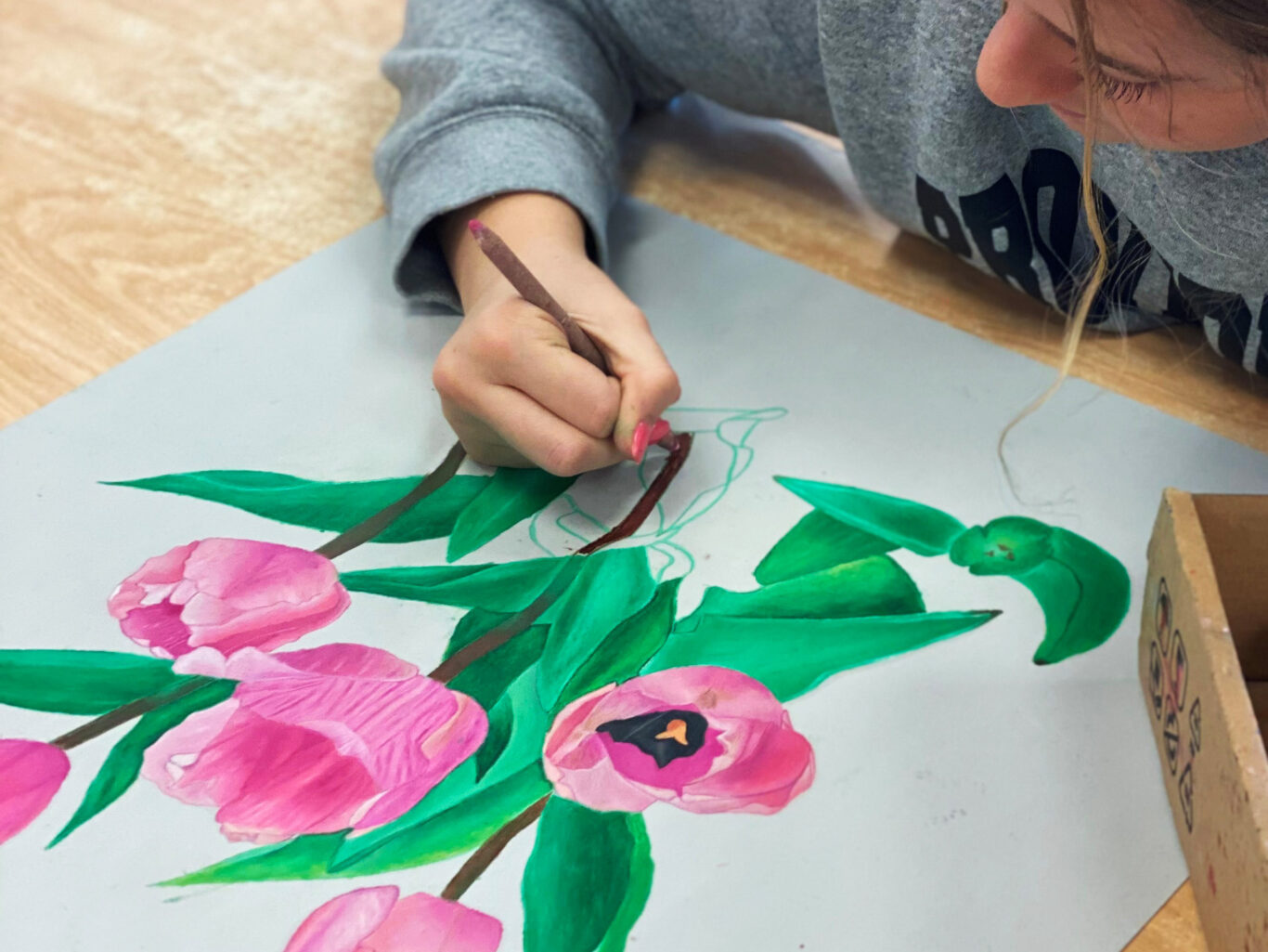 A girl creates visually captivating pink flowers on a piece of paper using her artistic skills in visual arts.