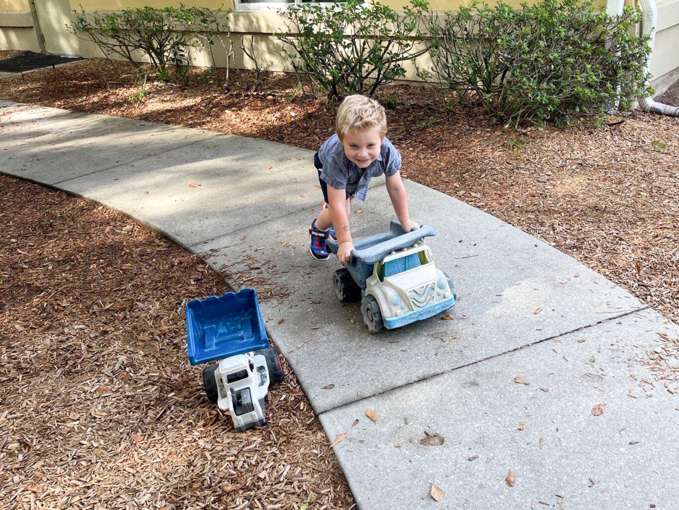 A preschool boy playing with a toy truck on a sidewalk.