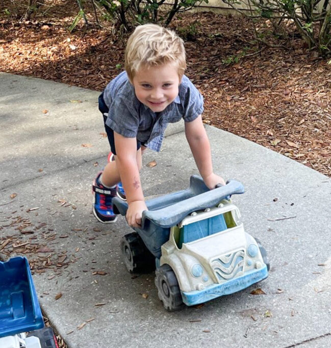 A preschool boy playing with a toy truck on a sidewalk.