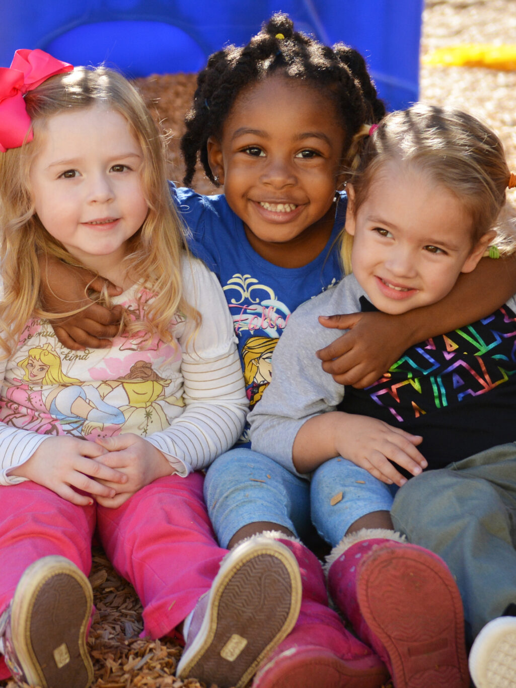 Three preschool children posing for a photo in front of a playground.