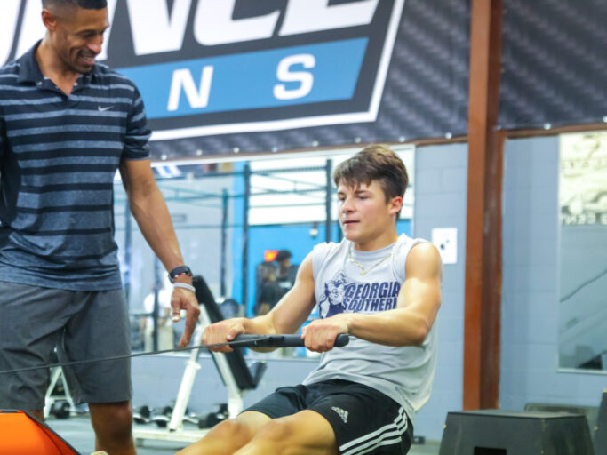 A young man is sitting on a rowing machine in a gym, embracing student life.