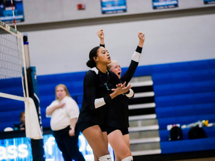 A volleyball player is raising her arms in the air, showcasing her athleticism.