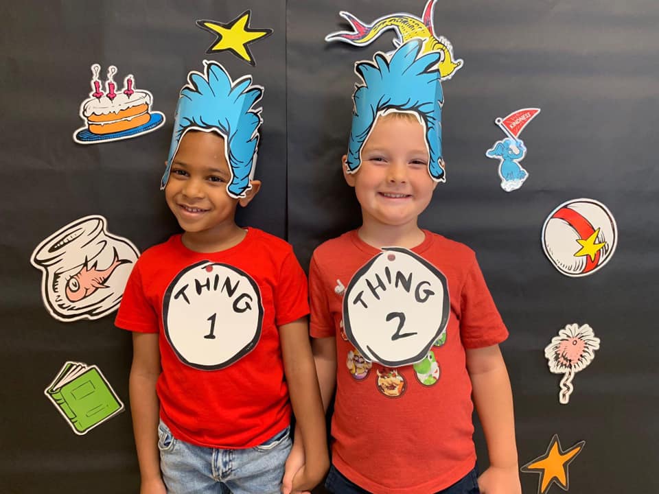 Two boys in dr seuss costumes standing in front of a bulletin board at an extracurricular event.