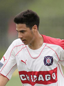 A young man in a red and white uniform, possibly a college or pro athlete, kicking a soccer ball.