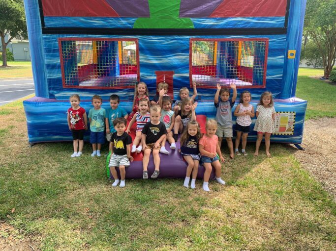 A group of children from a classroom posing in front of a bounce house.