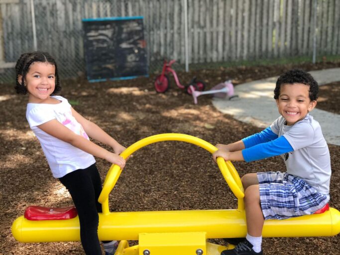 Two children playing on a yellow playground slide during recess.