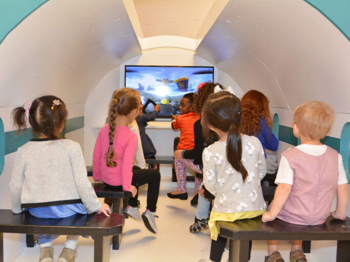 A group of children watching a TV in a classroom.