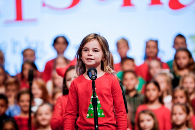 A young girl showcasing her impressive performing arts skills, captivating a crowd of people with her enchanting voice.