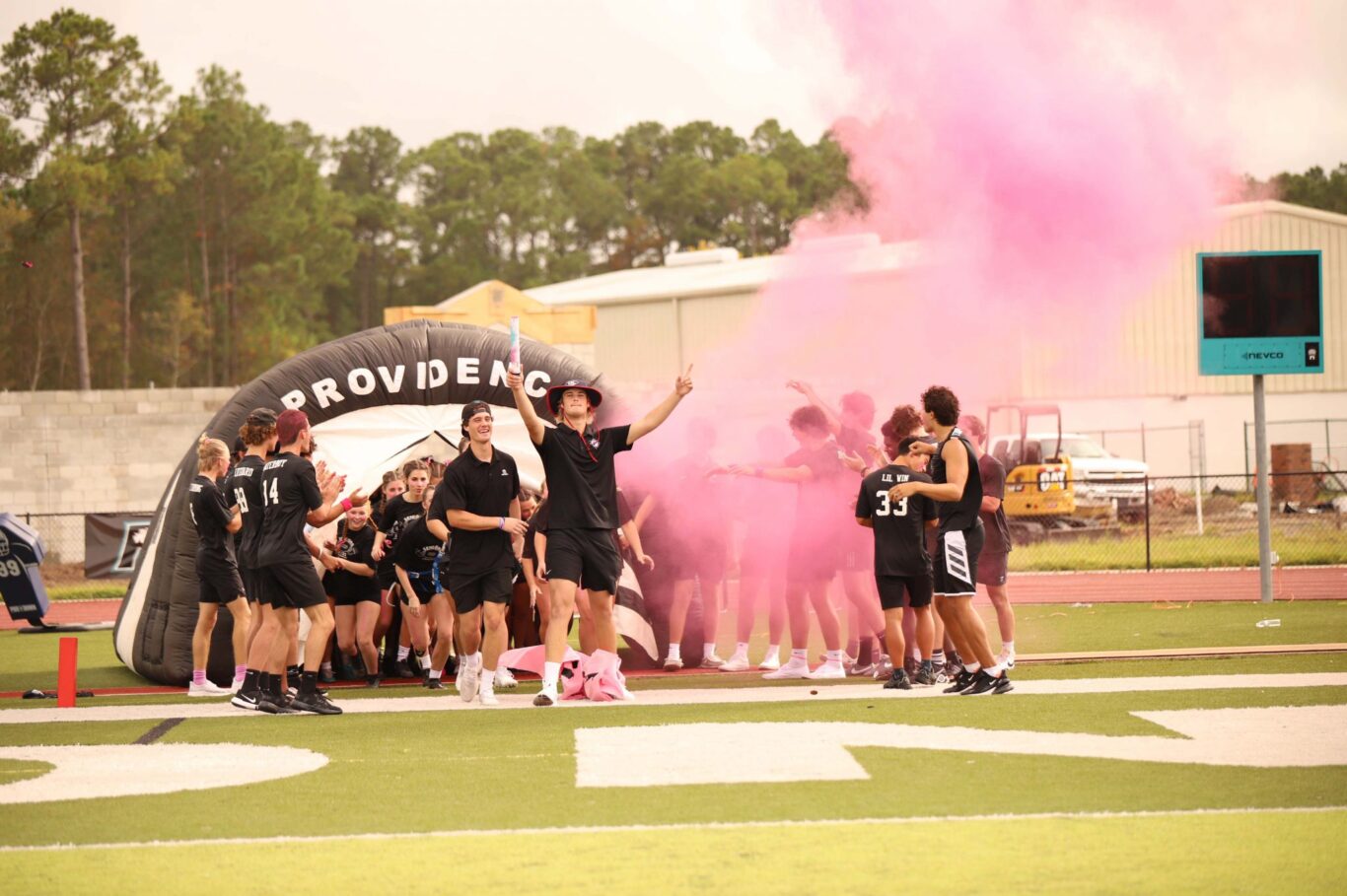 A group of girls standing on a field with pink smoke during 2023 Homecoming.