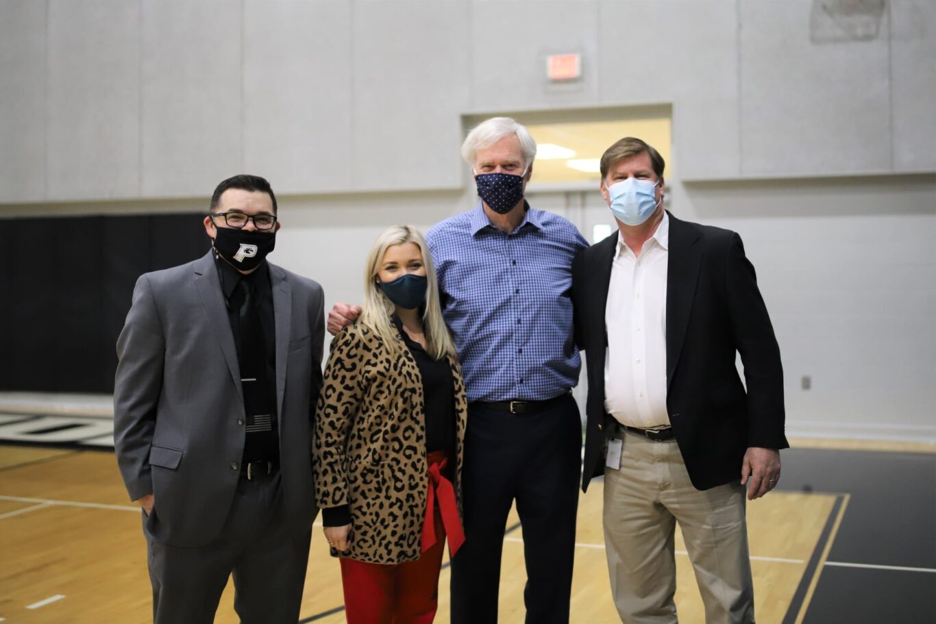Three people wearing face masks standing next to each other in a gym, practicing COVID-19 safety measures.