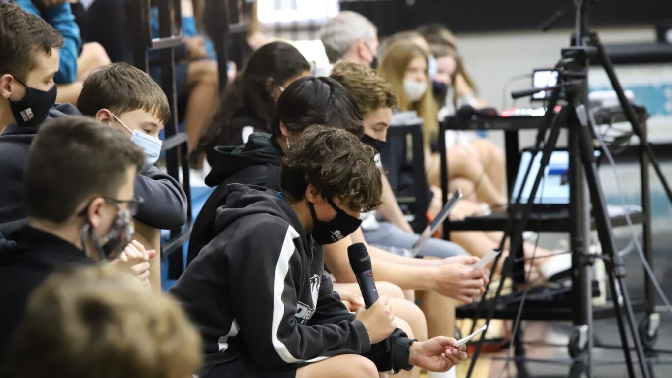 A group of people engaged in civic action, wearing masks, seated together in a gymnasium.