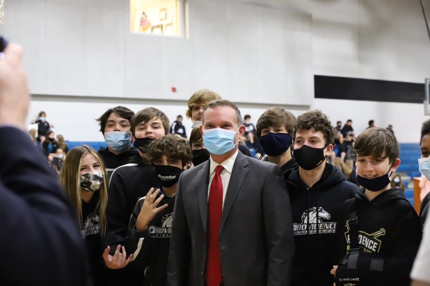 A man wearing a face mask takes action in front of a group of people.