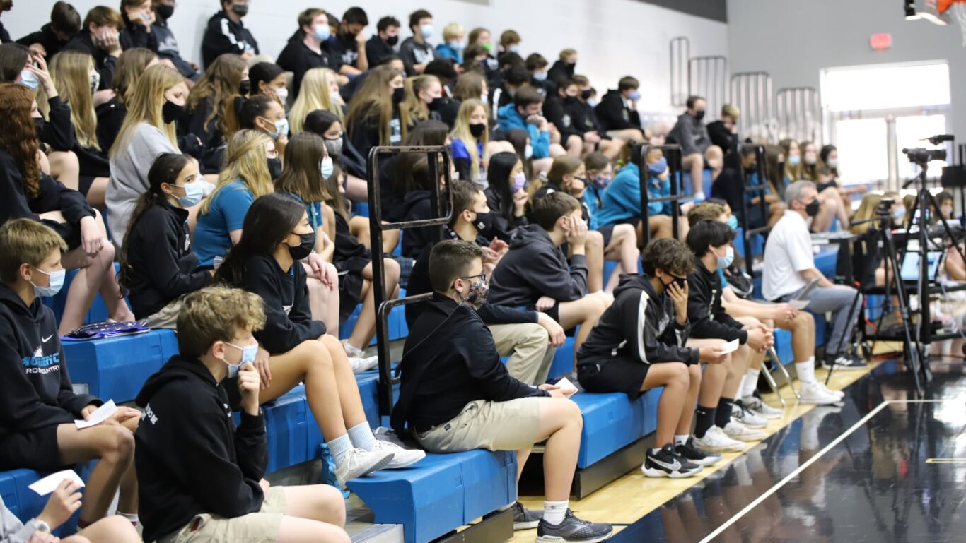 A group of people sitting on bleachers enthusiastically watching a basketball game.