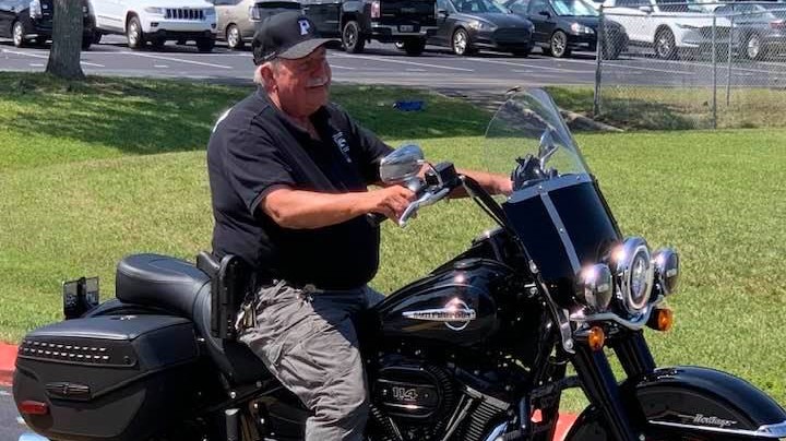 In Loving Memory, Mr. Larry, sits on a black motorcycle in a parking lot.