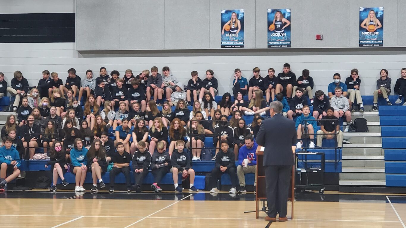 A man is facilitating a civics discussion with a group of people in a gym.