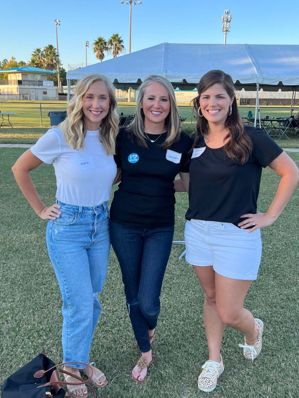 Three women posing for a Homecoming photo in a grassy field.