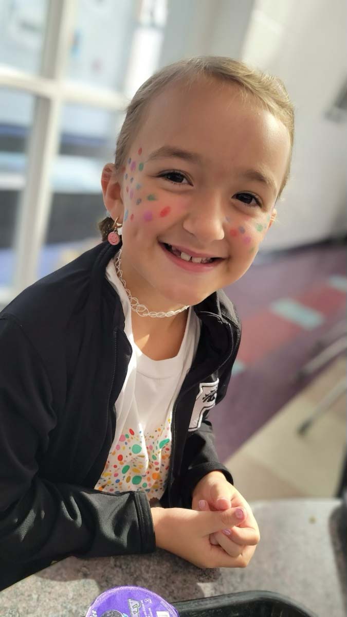 A young girl, smiling and adorned with face paint, celebrates an international event.