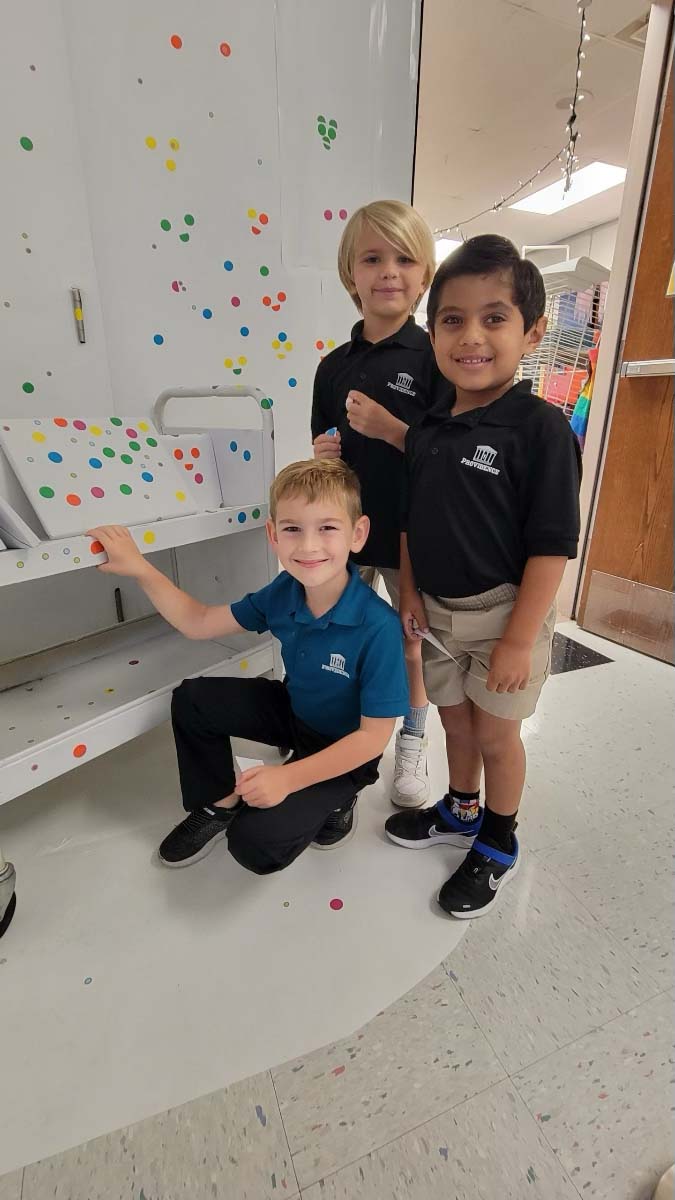 Three students celebrating International Dot Day, posing in front of a colorful wall.
