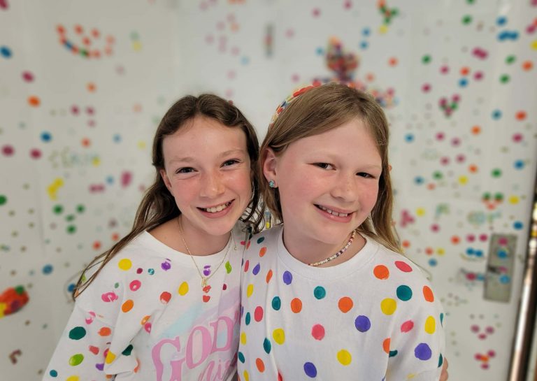 Two students in polka dot shirts celebrate International Dot Day as they stand in front of a polka dot wall.