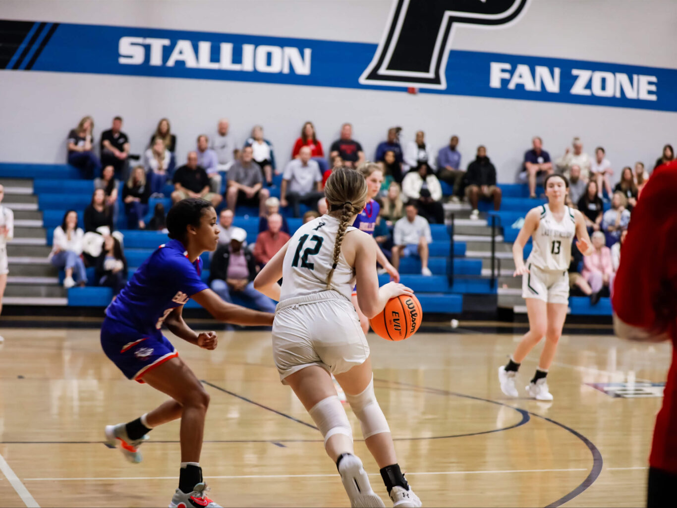 A Girls basketball player confidently dribbling in front of a crowd.
