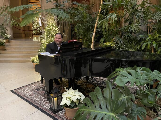 A man in a suit, from the Prov Chorale, playing a piano in the Carnegie lobby.