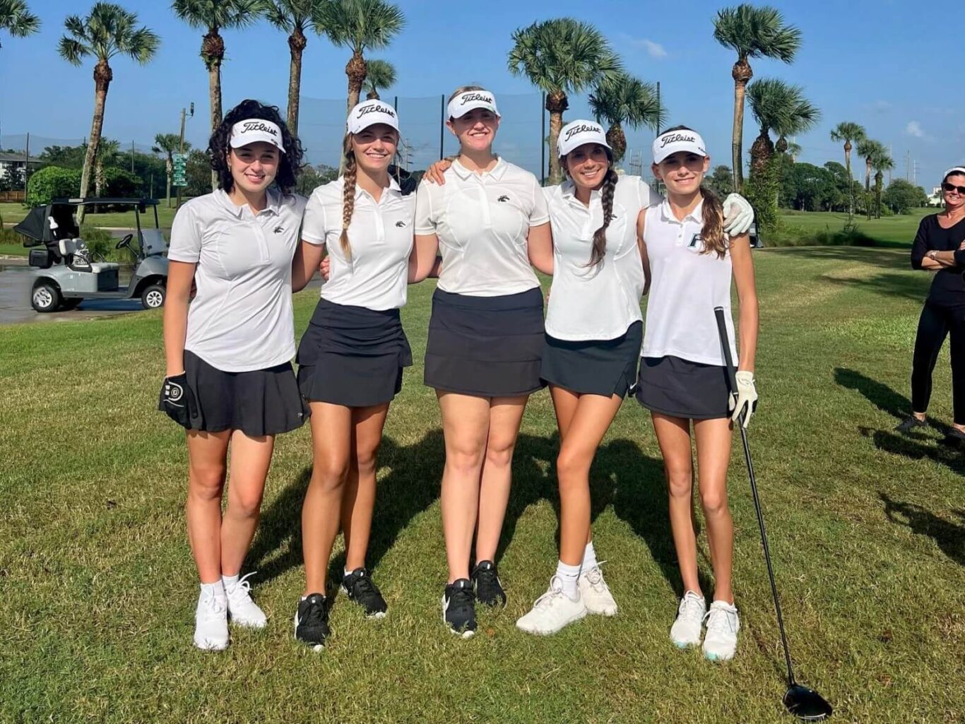 Four girls posing for a picture on a golf course.