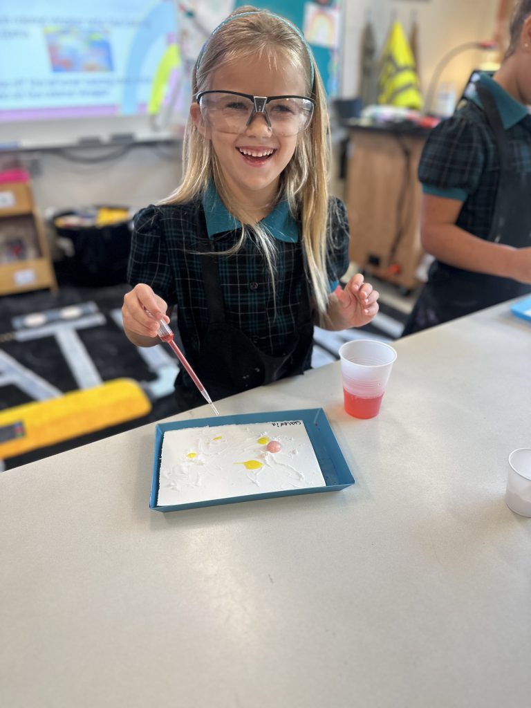 A Lower School girl in glasses is holding a tray of paint during a STEAM Discovery activity.